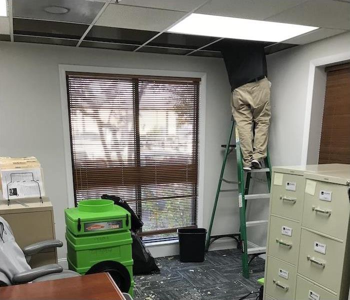 SERVPRO technician on a ladder working on a ceiling with water damage